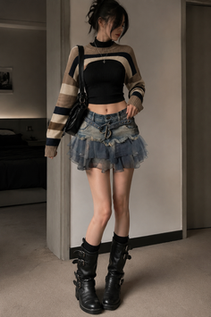 Woman in a cropped sweater, denim skirt, and black boots indoors