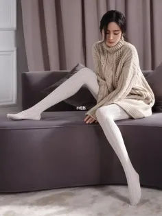 Woman in a beige turtleneck sweater and white tights sitting on a sofa