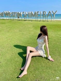 Woman in a floral dress sitting on grass with a beach in the background