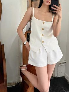Woman in a white top and shorts taking a mirror selfie indoors