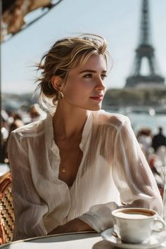 Woman with blonde hair in a sheer blouse at an outdoor cafe with the Eiffel Tower in the background