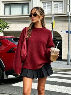 Woman in a red sweater and black pleated skirt holding a coffee cup on a street