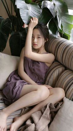 Young woman in a purple dress sitting on a striped couch indoors