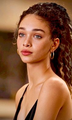 Woman with curly hair and freckles wearing a black top and hoop earrings