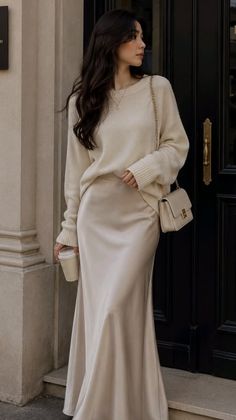 Woman in a cream sweater and satin skirt holding a coffee cup outdoors