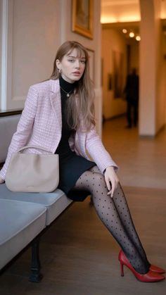 Woman in a pink blazer and polka dot tights sitting indoors