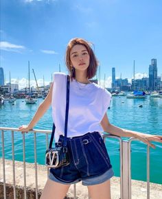 Woman in a white t-shirt and denim shorts posing by a harbor on a sunny day