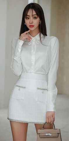 Woman in a white shirt and mini skirt holding a handbag indoors