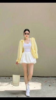 Woman in a yellow jacket, white tank top, and white shorts holding a bag