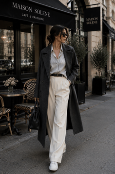 Woman in a long coat and wide leg pants walking past a cafe