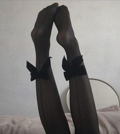 Legs in black stockings with bows, raised against a light wall