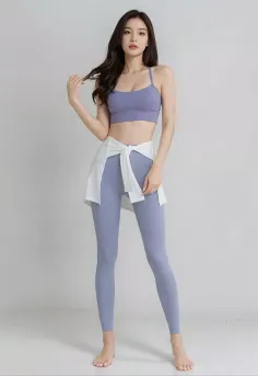Woman in a purple sports bra and leggings with a white shirt tied around her waist