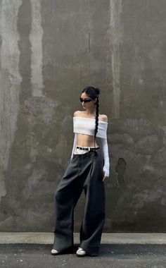 Woman in an off-shoulder crop top and wide-leg pants against a concrete wall