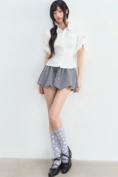 Woman with long black hair wearing a white shirt and grey skirt with polka dot socks