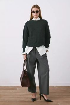 Woman in a dark sweater, white shirt, and wide leg pants holding a handbag