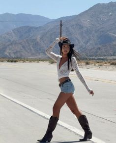 Woman in a cowboy hat, denim shorts, and boots on a desert road