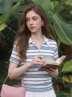 Woman with long hair wearing a striped shirt, holding a book outdoors
