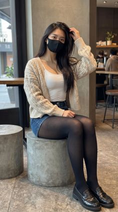 Woman with long hair and a black mask sitting indoors
