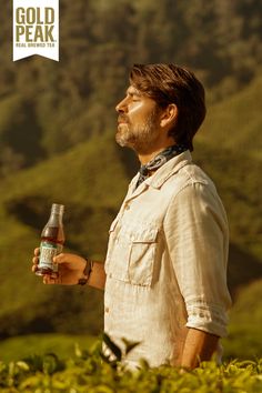 Man with a beard and bandana holding a bottle of Gold Peak tea in a tea plantation
