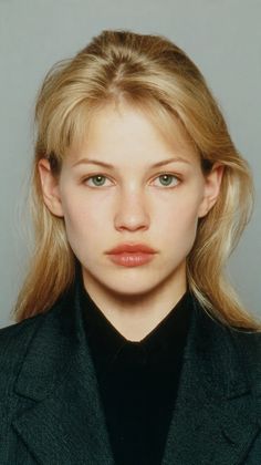 Blonde woman with green eyes wearing a dark blazer and black shirt in a studio