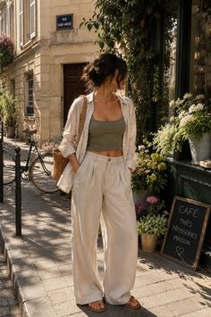 Woman in a crop top and loose pants standing on a sunny street in front of a cafe