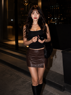 Woman in a black tank top and brown leather skirt holding a small box at night