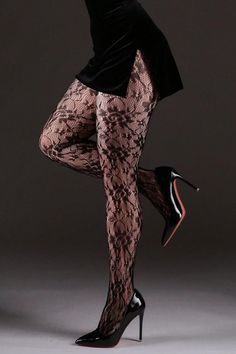 Woman in a black dress, lace tights, and high heels posing in a studio