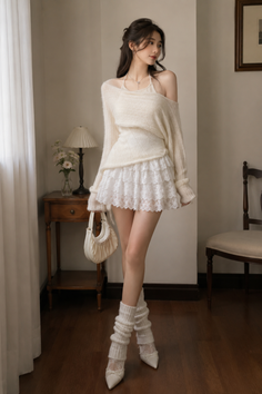 Woman in a white lace skirt and off-shoulder sweater posing indoors