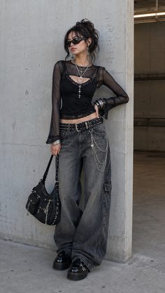 Woman in a black mesh top and baggy jeans with layered necklaces and sunglasses