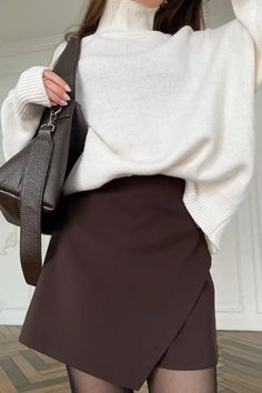 Woman in a white turtleneck sweater and brown mini skirt with a shoulder bag