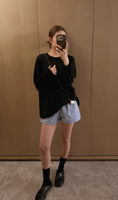 Woman in a black sweater and striped shorts taking a mirror selfie