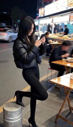 Woman in a black puffer jacket and leggings checking her phone at night