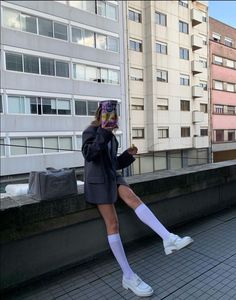 Person in an oversized blazer and white knee socks sitting on a ledge in a city