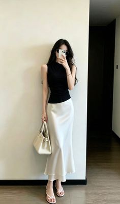 Woman in a black top and white skirt taking a mirror selfie indoors