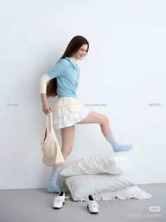Woman in a blue sweater and white skirt posing with pillows in a studio