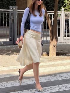 Woman in a light blue top and cream midi skirt walking on a zebra crossing