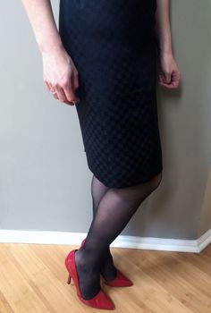 Woman in a black dress, black stockings, and red high heels indoors