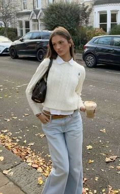 Woman in a white sweater and light wash jeans holding a coffee cup on a street