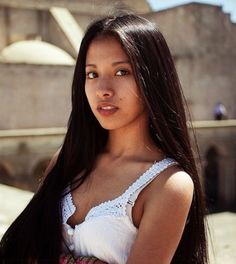Young woman with long dark hair wearing a white top outdoors