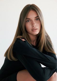 Woman with long brown hair wearing a black top against a white background