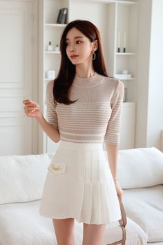 Woman with long hair wearing a striped top and white pleated skirt indoors