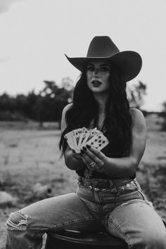 Woman in a cowboy hat and ripped jeans holding playing cards outdoors