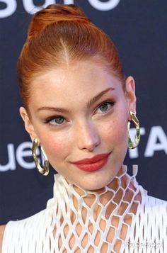 Woman with red hair in a bun wearing a white high-neck dress and gold earrings