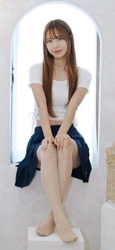 Woman with long hair in a white crop top and navy skirt sitting by a window