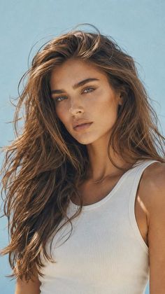 Woman with long brown hair and freckles wearing a white tank top outdoors