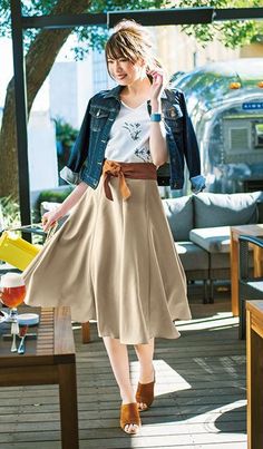 Woman in a denim jacket and midi skirt walking in an outdoor cafe