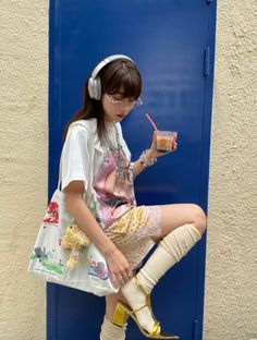 Woman with headphones and glasses holding a drink, wearing lace shorts and gold heels