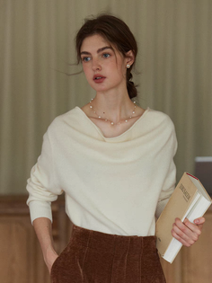 Woman with long hair wearing a white sweater and brown pants, holding a book