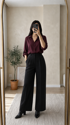 Woman in a burgundy shirt and black pants taking a mirror selfie indoors
