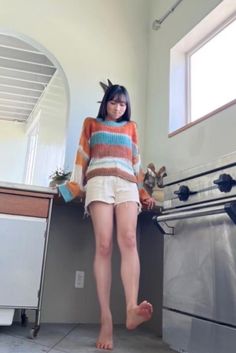 Woman in a striped sweater and shorts standing barefoot indoors
